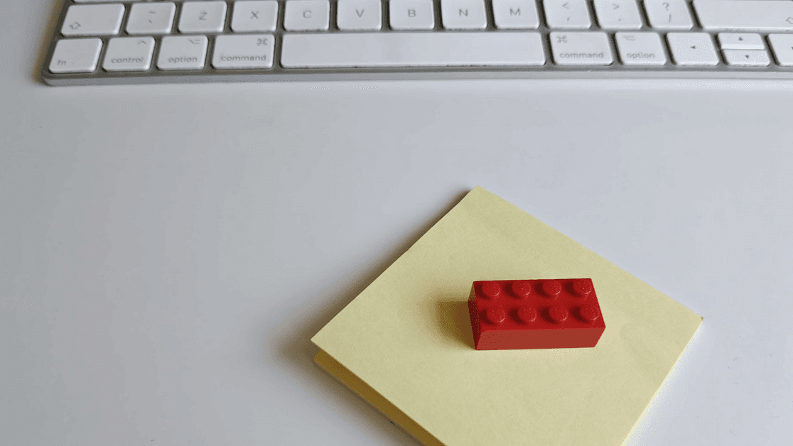 A red Lego brick on a yellow sticky note in front of a keyboard