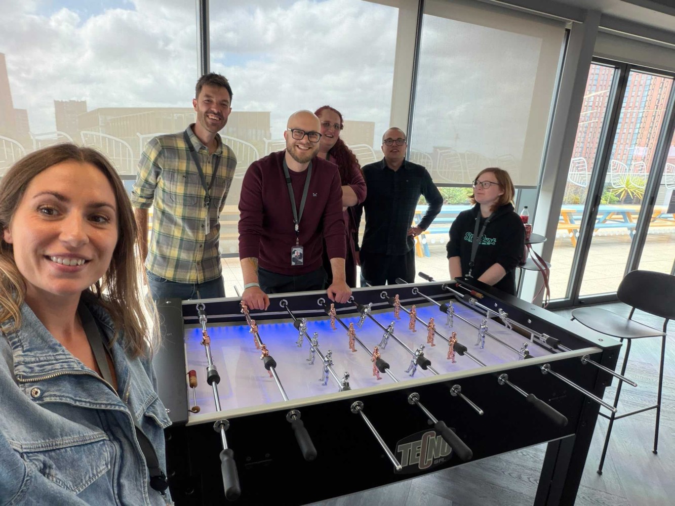 The team smiling around the office foosball table